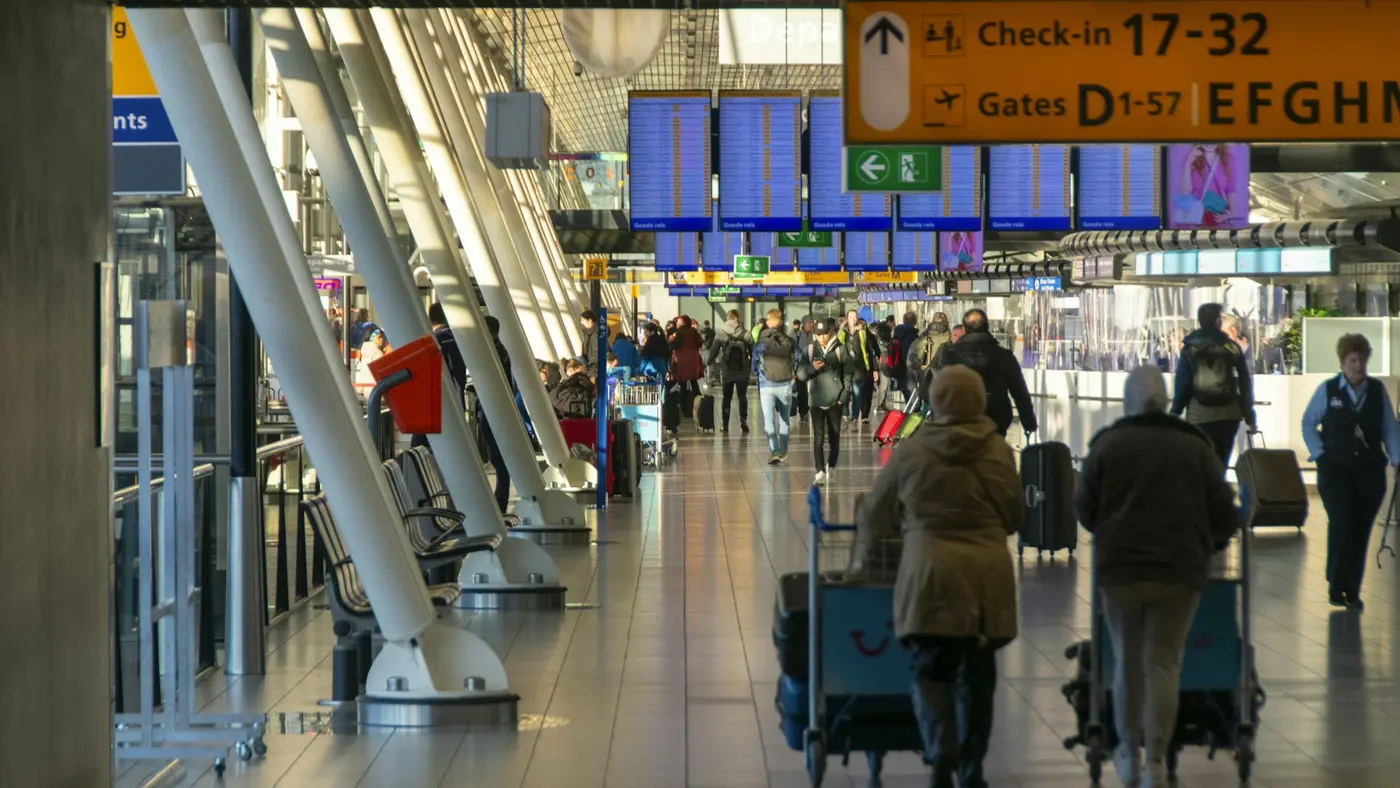 Travelers with luggage trolleys walking through an airport terminal under check-in and gate signs
